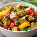 - 1 block of firm tofu, thoroughly drained and pressed - 1 red bell pepper, sliced into thin strips - 1 yellow bell pepper, sliced into thin strips - 1 cup snap peas, trimmed - 2 cloves garlic, finely minced - 1 tablespoon fresh ginger, minced - ¼ cup sweet chili sauce - 2 tablespoons soy sauce Tofu is the star of this dish. It soaks up flavors while giving a great texture. I prefer firm tofu for this recipe. It holds up well during cooking. Choose fresh, high-quality tofu for the best taste. Vegetables add color and crunch. I love using red and yellow bell peppers for their sweetness. Snap peas give a nice snap and freshness. You can mix and match other veggies based on your taste. Sauces bring everything together. Sweet chili sauce adds sweetness and a bit of heat. Soy sauce adds umami and saltiness. Together, they make a perfect blend for your stir-fry. - 2 tablespoons cornstarch - 2 tablespoons vegetable oil - 1 tablespoon sesame oil Cornstarch helps create a crispy layer on the tofu. It’s simple but effective. Tossing tofu in cornstarch before cooking makes it golden and crunchy. Vegetable oil is great for frying. It has a high smoke point, so it won’t burn. Sesame oil adds a nutty flavor at the end. Just a drizzle gives a lovely finish. - Chopped green onions, for garnish - Toasted sesame seeds, for garnish Green onions add a fresh bite. They also brighten the dish visually. Just chop them up and sprinkle on top before serving. Toasted sesame seeds add a crunchy texture. They give a nice nutty flavor too. A sprinkle of these seeds makes your stir-fry look fancy. {{ingredient_image_2}} To start, you need to cut the tofu. Chop it into 1-inch cubes. This size works best for frying. Next, press the tofu to remove excess water. You can use a clean kitchen towel for this. Place the towel on a plate and set another plate on top of the tofu. Let it sit for about 15 minutes. This step helps the tofu absorb flavors and stay crispy. Now, toss the tofu cubes in a bowl with cornstarch. Make sure each piece is well-coated. This coating gives the tofu its crispy texture when you fry it. In a large skillet or wok, heat vegetable oil over medium-high heat. You want the oil to shimmer; this means it's ready for cooking. Carefully add the cornstarch-coated tofu. Cook it for 8-10 minutes. Turn the tofu cubes often, so they brown evenly. When they are golden and crispy, take them out and place them on a paper towel-lined plate. This helps absorb extra oil. Now, use the same pan for the veggies. Add the sliced red and yellow bell peppers along with the snap peas. Stir-fry these colorful vegetables for about 3-4 minutes. You want them to soften but still be crunchy. Next, add the minced garlic and ginger. Stir everything together for 1-2 minutes. The garlic and ginger will fill your kitchen with a lovely aroma. Return the crispy tofu to the pan with the veggies. Pour in the sweet chili sauce and soy sauce. Gently toss everything to coat the tofu and vegetables well in the sauce. The sweet and savory flavors will blend nicely. Drizzle sesame oil over the stir-fry. Toss it all for one more minute. This step adds a rich flavor. Finally, remove the pan from heat. Garnish with chopped green onions and toasted sesame seeds. These toppings add a nice crunch and flavor. Enjoy your colorful and tasty Sweet Chili Tofu Stir-Fry! Pressing tofu is key to getting it crispy. When you press tofu, you remove excess water. This step lets the tofu absorb more flavors and helps it fry better. I use a clean towel and a heavy object to press it for about 30 minutes. Cook tofu at the right temperature. Heat your oil until it shimmers. This means it’s hot enough to fry the tofu. If the oil isn’t hot enough, the tofu will soak up oil and become soggy. For stir-frying, I love using bell peppers and snap peas. They add color and crunch. Other great options include broccoli, carrots, and zucchini. Use a mix of your favorites for a vibrant dish. Timing is crucial for perfect crunch. Add the veggies to the pan after the tofu. Stir-fry them for just a few minutes, until they soften but still have a bite. This keeps your stir-fry fresh and tasty. You can adjust the sweetness and spice of your sauce. If you like it sweeter, add more sweet chili sauce. To make it spicier, add a pinch of red pepper flakes or a splash of sriracha. If you want to switch things up, try other sauces. Teriyaki or hoisin sauce can add a fun twist. You can even mix your own sauce with soy sauce and ginger for a unique flavor. Pro Tips Press Tofu Thoroughly: Ensure your tofu is well-pressed to remove excess moisture, which helps achieve a crispy texture when frying. Use High Heat: Cooking the tofu on medium-high heat allows it to crisp up quickly, giving it a delightful texture that complements the stir-fry. Customize Vegetables: Feel free to mix and match your favorite vegetables in this stir-fry, such as broccoli, carrots, or zucchini, for added nutrition and flavor. Serve Immediately: For the best texture and flavor, serve the stir-fry right after cooking, as the tofu can lose its crispiness if it sits too long. {{image_4}} You can switch tofu for tempeh or chicken. Tempeh gives a nutty flavor and a firmer bite. Chicken adds a hearty touch and cooks quickly. For a non-vegetarian option, add shrimp. Shrimp cooks fast and pairs well with sweet chili sauce. Feel free to mix in other vegetables. Broccoli, carrots, or zucchini work great. You can also use seasonal vegetables. Asparagus in spring or squash in fall can add new tastes and colors to your dish. Making your own sweet chili sauce is easy. Combine sugar, vinegar, and chili flakes for a fresh taste. You can also experiment with different marinades. Try adding lime juice or garlic for a unique twist. Mixing sauces can enhance the flavor profile of your stir-fry. To store leftovers, let the stir-fry cool down first. Then, place it in an airtight container. This helps keep the flavors fresh. I recommend using glass or BPA-free plastic containers. They are great for storing food. You can also reuse old jars or takeout containers if they seal well. Freezing tofu stir-fry is easy. To do this, let it cool completely. Then, transfer it to freezer-safe bags or containers. Make sure to remove as much air as possible to avoid freezer burn. When you want to eat it, thaw it overnight in the fridge. Reheat it on the stove over low heat. Stir occasionally to warm it through without overcooking. In the fridge, this dish lasts about 3 to 4 days. Keep an eye out for signs of spoilage. If you see mold or an off smell, it’s best to toss it out. Freshness is key for enjoying your sweet chili tofu stir-fry! Yes, you can make this dish gluten-free. To do this, use gluten-free soy sauce. Look for brands labeled as gluten-free. Tamari is a great option, as it is naturally gluten-free. This way, you can enjoy the same sweet and salty taste without the gluten. You can serve this stir-fry with many side dishes. Fluffy jasmine rice pairs well and absorbs the sauce nicely. Quinoa is another healthy choice that adds protein. You can also try serving it with steamed broccoli or a fresh salad for extra crunch. Yes, frozen vegetables work well in this recipe. They are quick and easy to use. Just add them straight to the pan without thawing. Cook them a bit longer to make sure they heat through. This saves time and still gives you a tasty dish. Absolutely! This stir-fry is great for meal prep. Cook it ahead of time and store it in containers. It lasts for about 4 days in the fridge. To reheat, just warm it in the microwave or on the stove. This makes busy days so much easier! This post covered how to make a tasty Sweet Chili Tofu Stir-Fry. You learned about the main ingredients like tofu and vegetables, plus important pantry staples. I provided step-by-step instructions for cooking crispy tofu and stir-frying veggies. You also got tips for customizing flavors and storage advice. Remember, this dish can change with different proteins and sauces. Enjoy creating your own version! With practice, you'll master this easy and delicious meal.